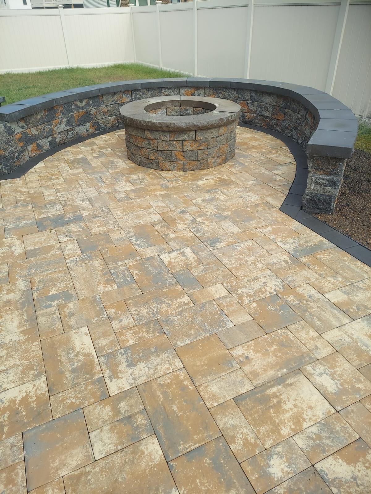 Tan paver patio with fire pit and curved seat wall by Kaeler