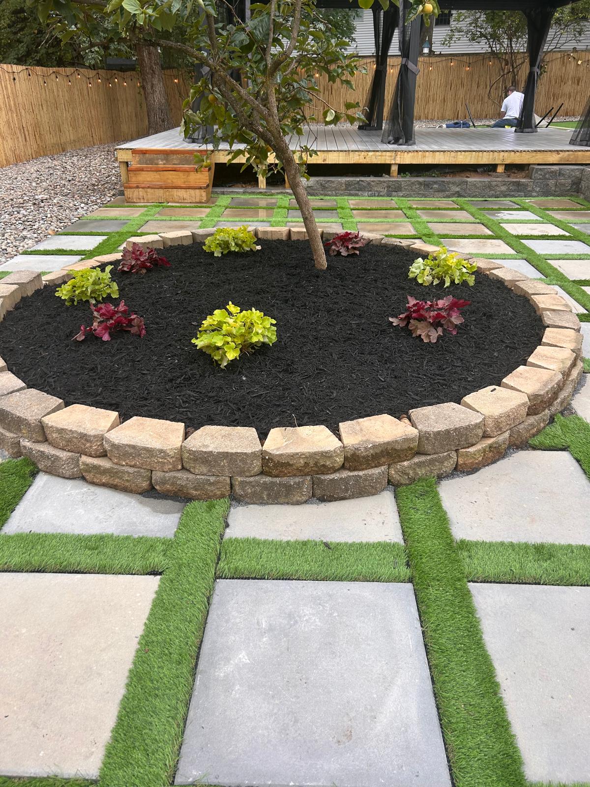 New plantings ringing a tree on a fresh paver patio by Kaeler